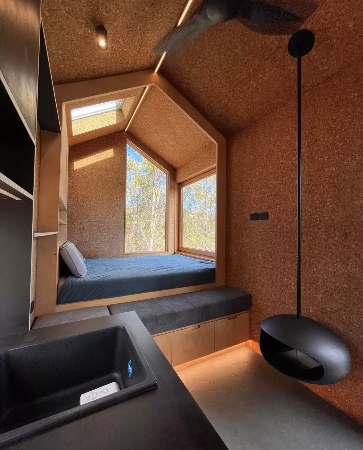 Compact cork-clad room with a bed & modern fan