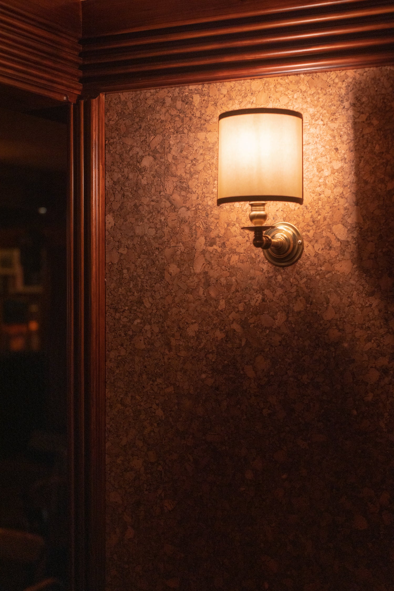 Wall sconce light fixture on cork wall with wooden trim in a dimly lit room